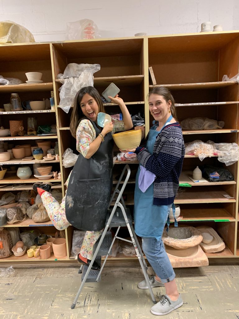 Elisenda Llaurado and Kaila Elders pose with ceramic pieces in a pottery studio