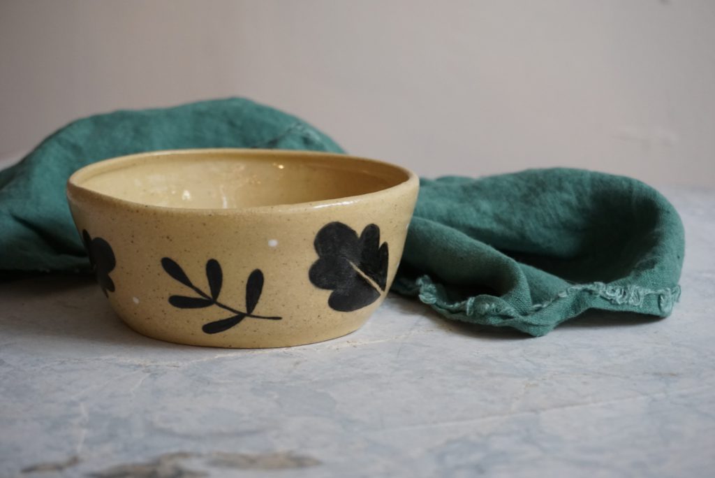A handmade ceramic bowl with a leaf pattern sits next to a green linen napkin