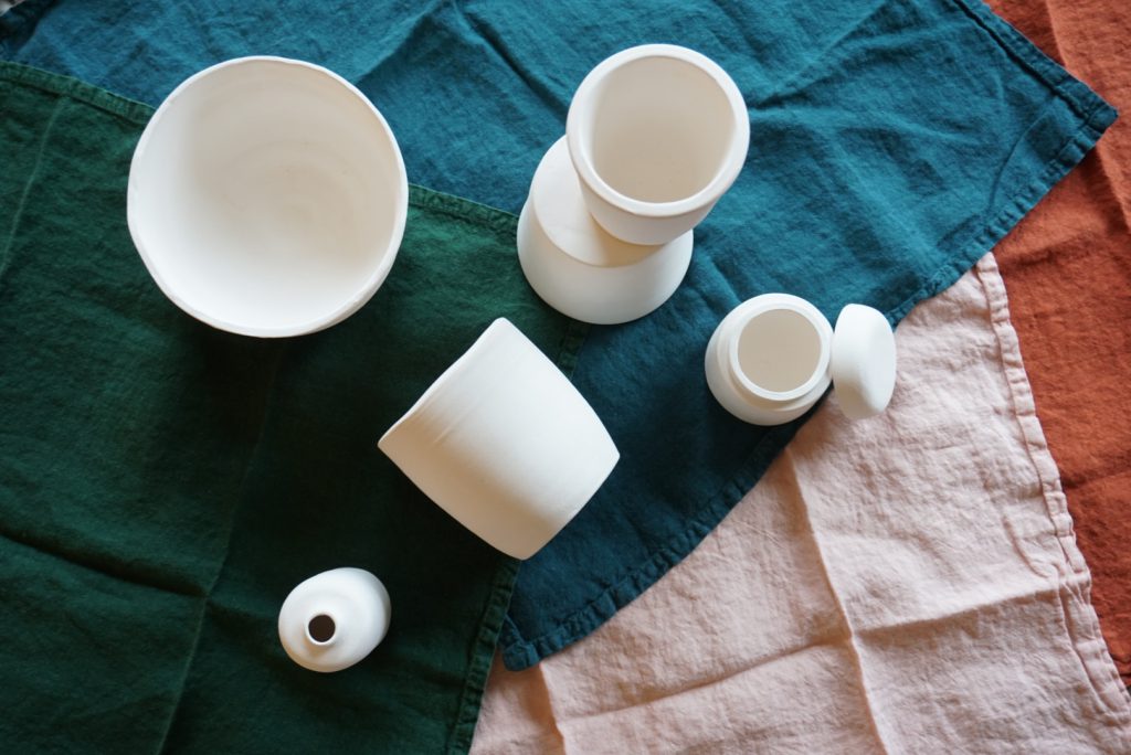 A collection of unglazed ceramic vessels atop colourful linen napkins