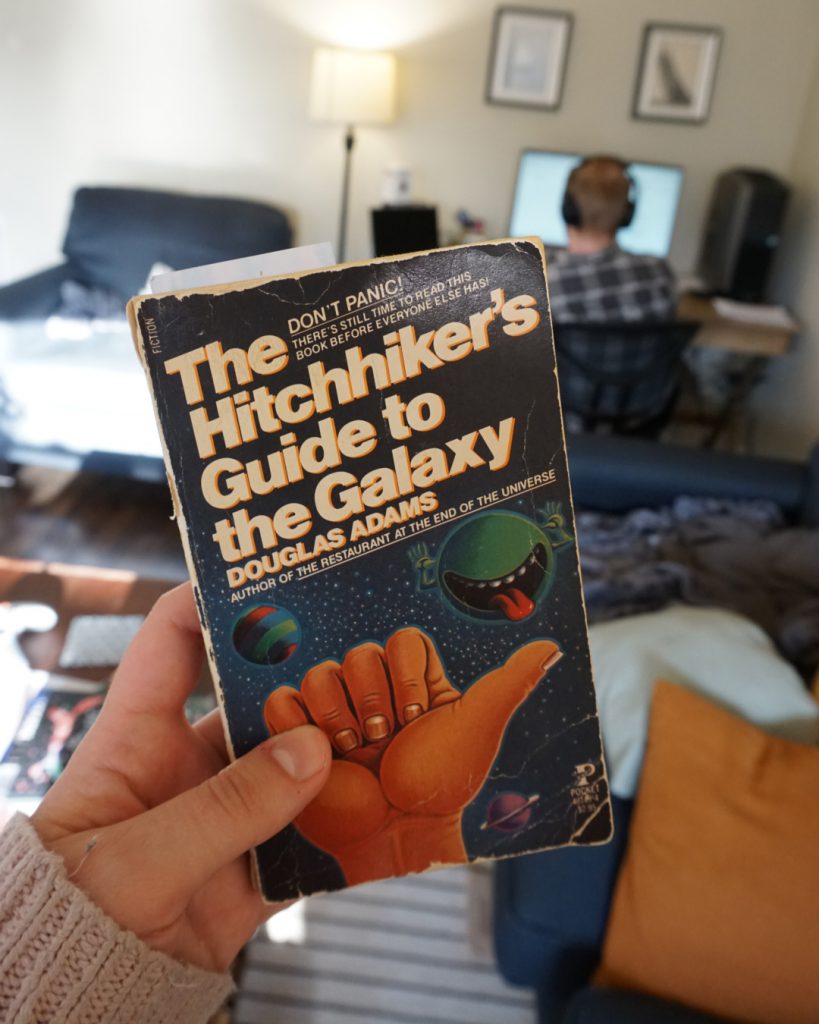 A hand holds a copy of Hitchhiker's Guide to the Galaxy