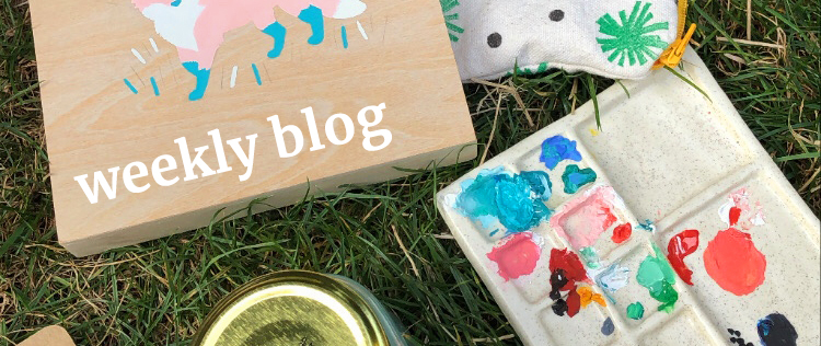 Painting supplies in the grass with the words Weekly Blog written across them