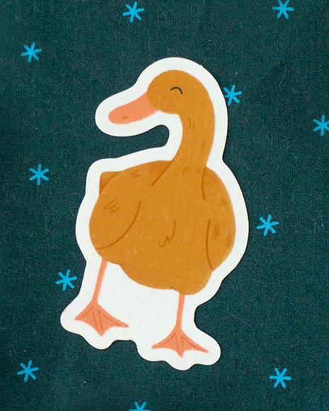 A brightly coloured orange duck sticker rests on teal fabric with blue stars on it.